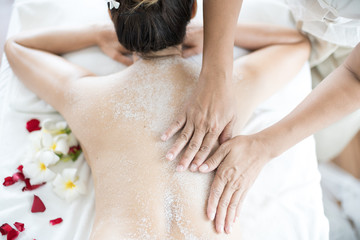 Close up. Asian woman massaging spa with salt. Beauty therapist pouring salt scrub on woman back at health spa.