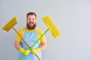 Funny fat man with a beard in an apron cleans up on a gray background.