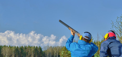 athlete shoots at clay pigeon under the guidance of a shooting coach, panoramic banner , Copy Space