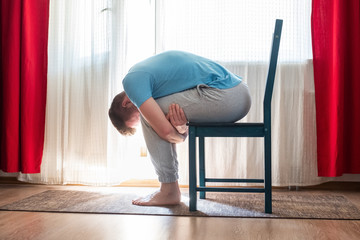 mature man doing childs pose in yoga using chair