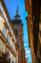 Fototapeta premium Low angle view on of facades of houses and the bell tower of the German church at old street in Gamla Stan in Stockholm, Sweden