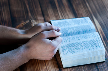 Naklejka premium Open bible on a wooden table. Hands of a praying man.
