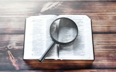 Open bible on a wooden table. Magnifier