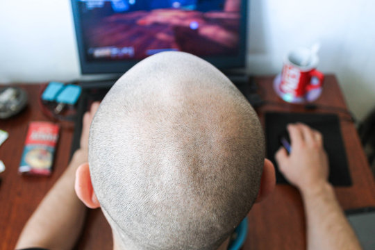 Rear view of a bald man playing a computer game.