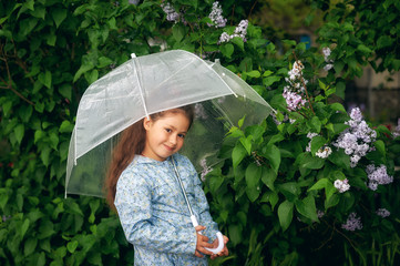 Portrait of a little girl with an umbrella at the blooming lilac