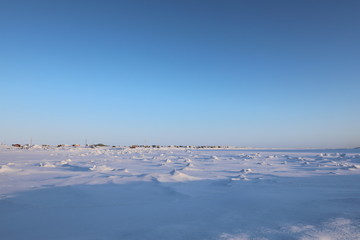 Fototapeta na wymiar Winter view of an isolated arctic community with snow and ice in the foreground and blue skies in the background, in Arviat, Nunavut Canada