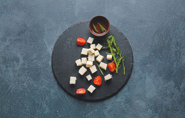 Slate plate with tasty cut feta cheese, tomatoes and herbs on table