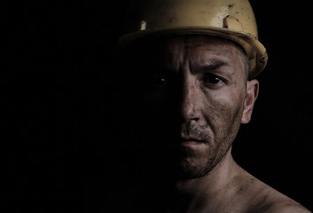 Miner in a yellow hard hat on a black background dirty with coal dust. - obrazy, fototapety, plakaty