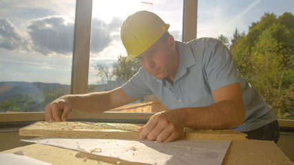 CLOSE UP: Handyman tosses a plank on workbench and measures it with tape measure