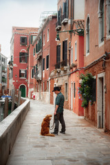 A man with a dog on a waterfront in Venice. Traveling with a pet. Nova Scotia Duck Tolling Retriever with the city