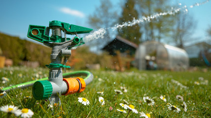 CLOSE UP: Irrigation system sprays a blooming meadow with refreshing rainwater.