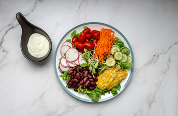 bowl of salad with vegetables ,fresh green oak salad, tomatoes, corn, Red beans, Carrot , red radish, olive oil and cucumber on white marble table. Top view. Food Concept for healthy diet