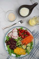 bowl of salad with vegetables ,fresh green oak salad, tomatoes, corn, Red beans, Carrot , red radish, olive oil and cucumber on white marble table. Top view. Food Concept for healthy diet