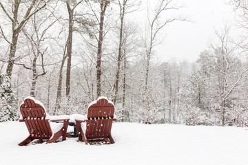 Snowy winter day with snow covering two adirondack chairs in the backyard.