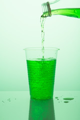 pouring green soda into a plastic glass, on a greenish background