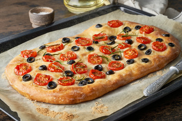 Focaccia, pizza, italian flat bread with tomatoes, olives and rosemary on tray