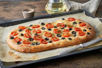 Focaccia, pizza, italian flat bread with tomatoes, olives and rosemary on tray