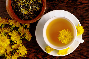 Dandelion tea with a fresh yellow flower inside a cup, on wooden background. Vitamin drink. Dandelion herbal tea for health.