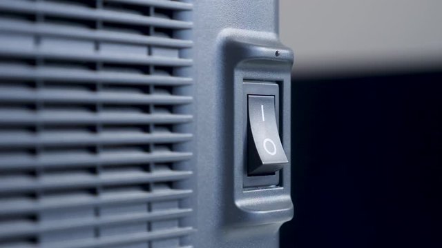 finger of a person presses turns on and off on a black plastic button a swing printer device with a radiator