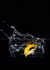 Lemon slice splashing water with tinny drops on the black backgound.
