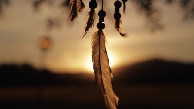 Dream catcher feather twisting at golden sunset. Slow motion shot on a gimbal