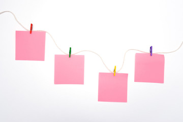 Pink blank paper stickers hang on a rope with color wooden clothespins on a white background.Copy space for notes