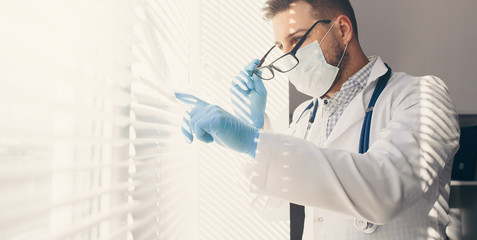 Young doctor look on window in mask and gloves