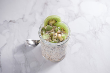 Overnight oats with chia seeds, kiwi and yogurt, on a white marble background.