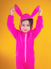 Cute girl in bright fuchsia costume or overalls pulling bunny ears and looking at camera against...