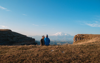 Naklejka premium Girl and dog on the background of Elbrus. A girl and a German shepherd travel through the mountains together.