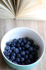 Bowl of fresh blueberries and open book on a table. Selective focus.