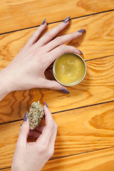 Self employed entrepreneur shows tin of home made self care beauty product in metal tin full of natural organic cannabis marijuana skin balm oil for homeopathic massage CBD THC pain relief 