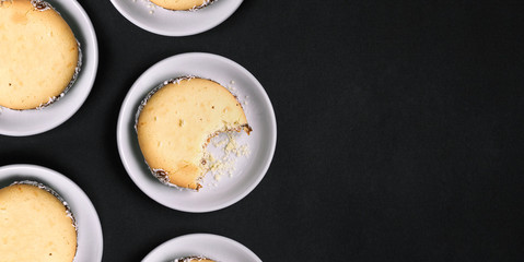 Sweet handmade cookies on a black background. One cookie bitten off. White plates with confectionery. Top view, copy space