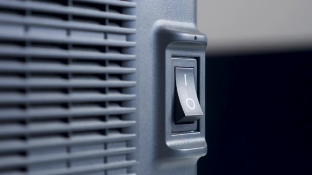 finger of a person presses turns on and off on a black plastic button a swing printer device with a radiator