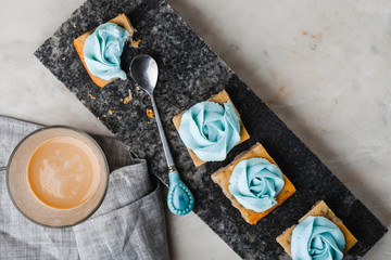 Cakes with cream on a granite tray, a glass of coffee with milk, a spoon on a marble table. Light dessert.