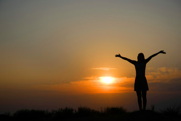 Silhouette of a girl on top of a mountain at sunset.