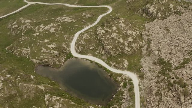 cinematic aerial view gravel trail road near small lake on the mountain. Cloudy weater, mist and haze. Forward dolly
