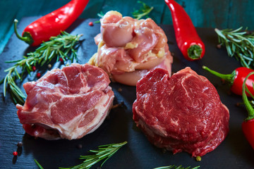 Fresh three types of meat chicken, pork and beef on black stone with herbs and pepper