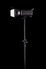 Photography studio flash on a lighting stand isolated on black background.