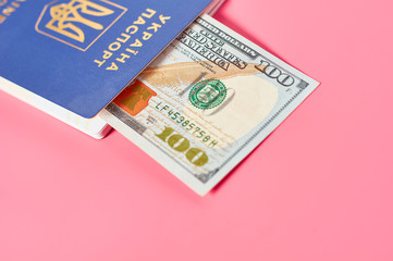 Fototapeta premium Passport of ukrainian citizen near banknote of 100 dollars on pink background. Concept of travel, donation or social payments