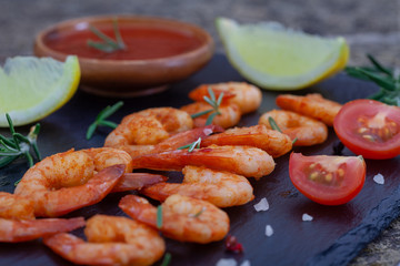 Delicious sauteed shrimps with sauce and lemon on black plate. Grilled tiger shrimps with rosemary and lspices.