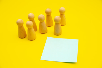 Teamwork, teambuilding mockup, company structure. Wooden figures stands over isolated yellow background near blue sticky note, place for text.