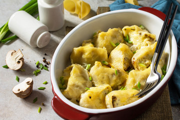 Italian pasta Conchiglioni Rigati stuffed with chicken, royal champignons, baked with cheese in bechamel sauce on a gray stone countertop.