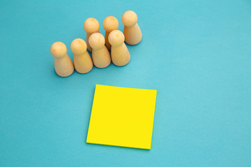 Teamwork, teambuilding mockup, company structure. Wooden figures stands near yellow sticky note, place for text.