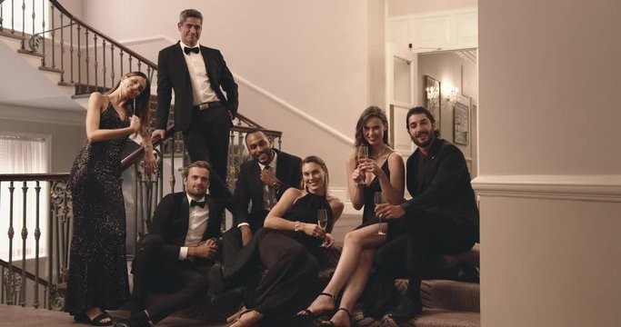 Group of men and woman sitting at stairs and looking at camera. Multi-ethnic friends enjoying at gala night.

