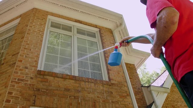 Man washing windows of the house with a power wash soap sprayer. Spring cleaning with hose and pressure washer. Cleaning service using a high pressure water jet to clean the facade of house.