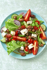 Healthy Salad with Tomatoes, Cucumber, Lettuce and Olives on bright wooden Background. Healthy Snack Idea. Top view.
