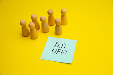 Wooden pawns with blue sticky note "Day off" on yellow background.
