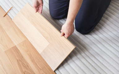 Installing laminated floor, detail on man hands fitting wooden tile, over white foam base layer