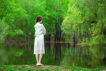 Portrait of a young beautiful woman in white dress posing by the lake